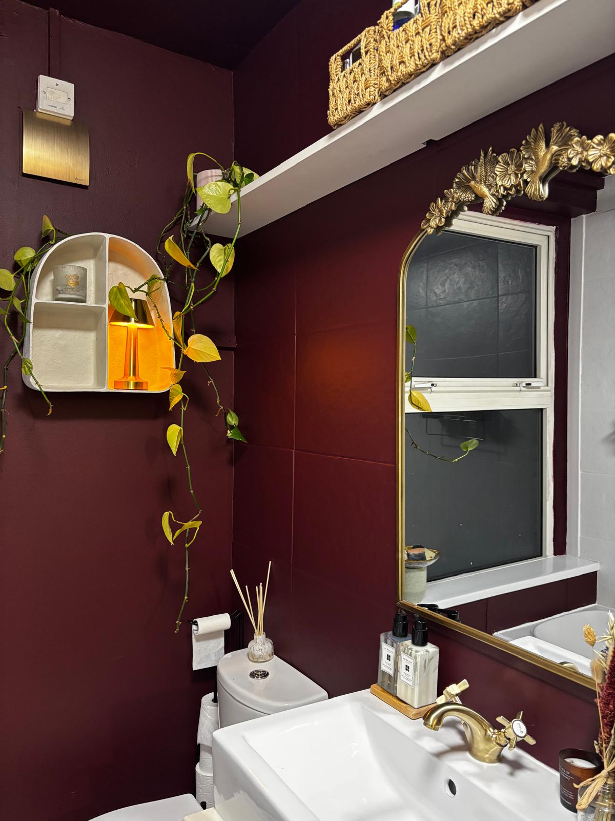 After: the bathroom decorated in deep burgundy with a gold-framed mirror and new tap.