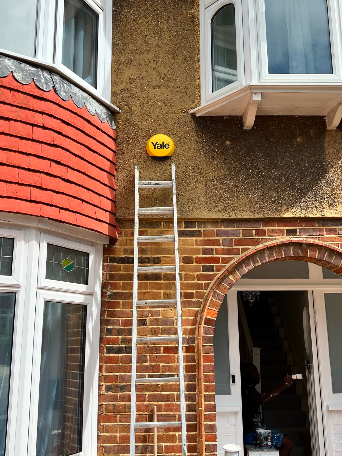 A yellow alarm box being fitted to the exterior wall of a house.