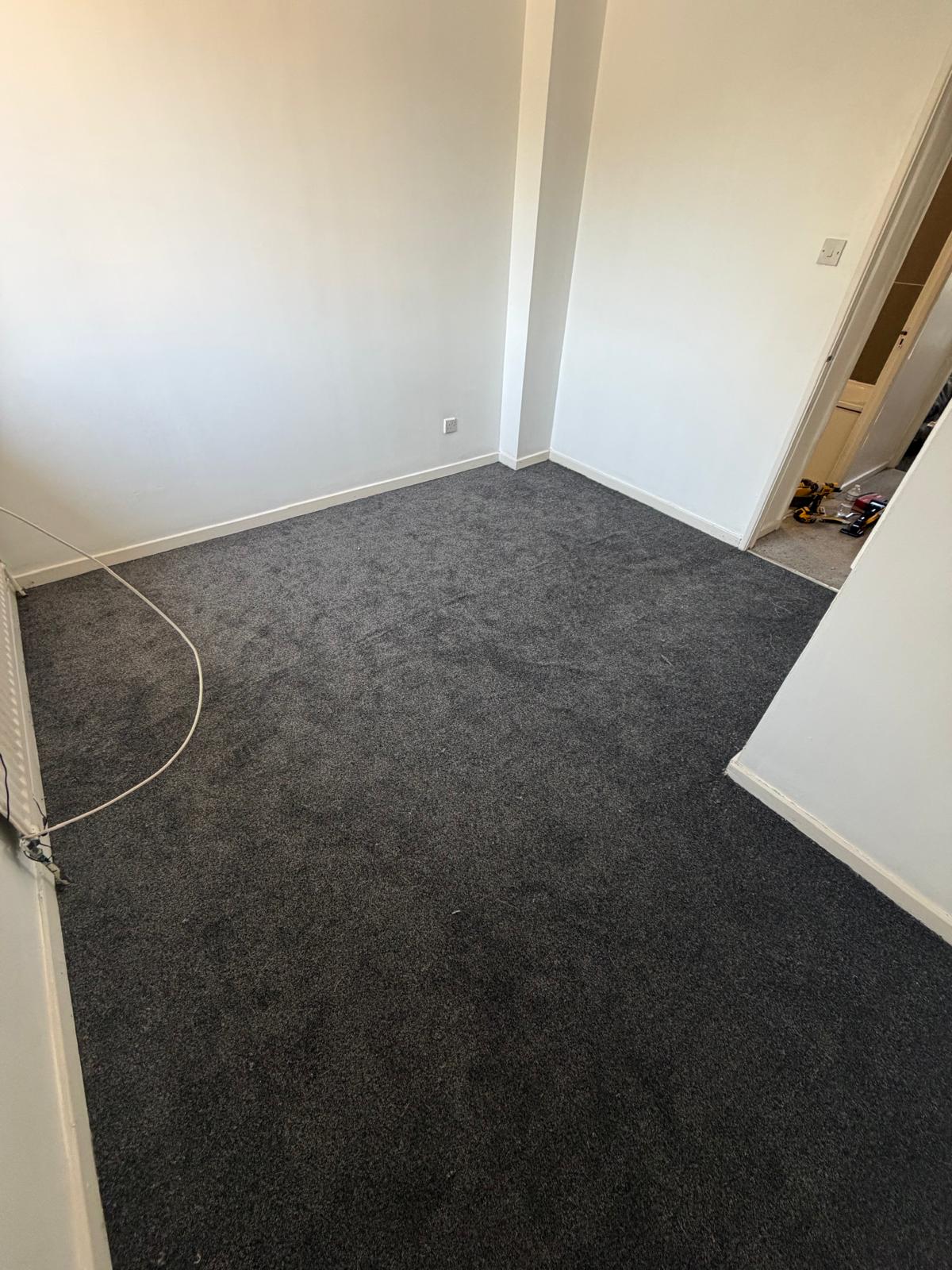 A room with newly laid dark grey carpet.