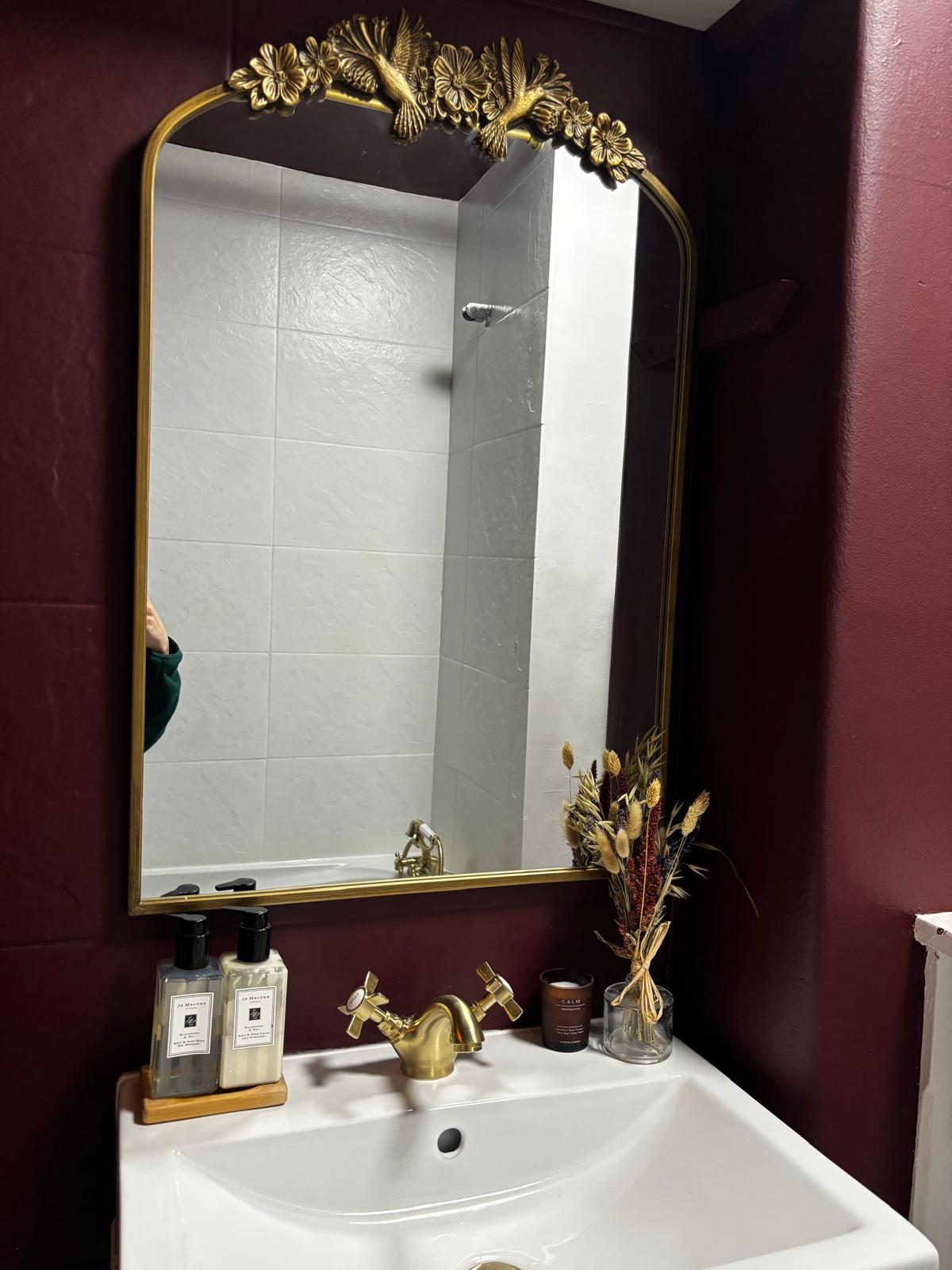 A white basin with gold taps below a decorative gold-framed mirror.
