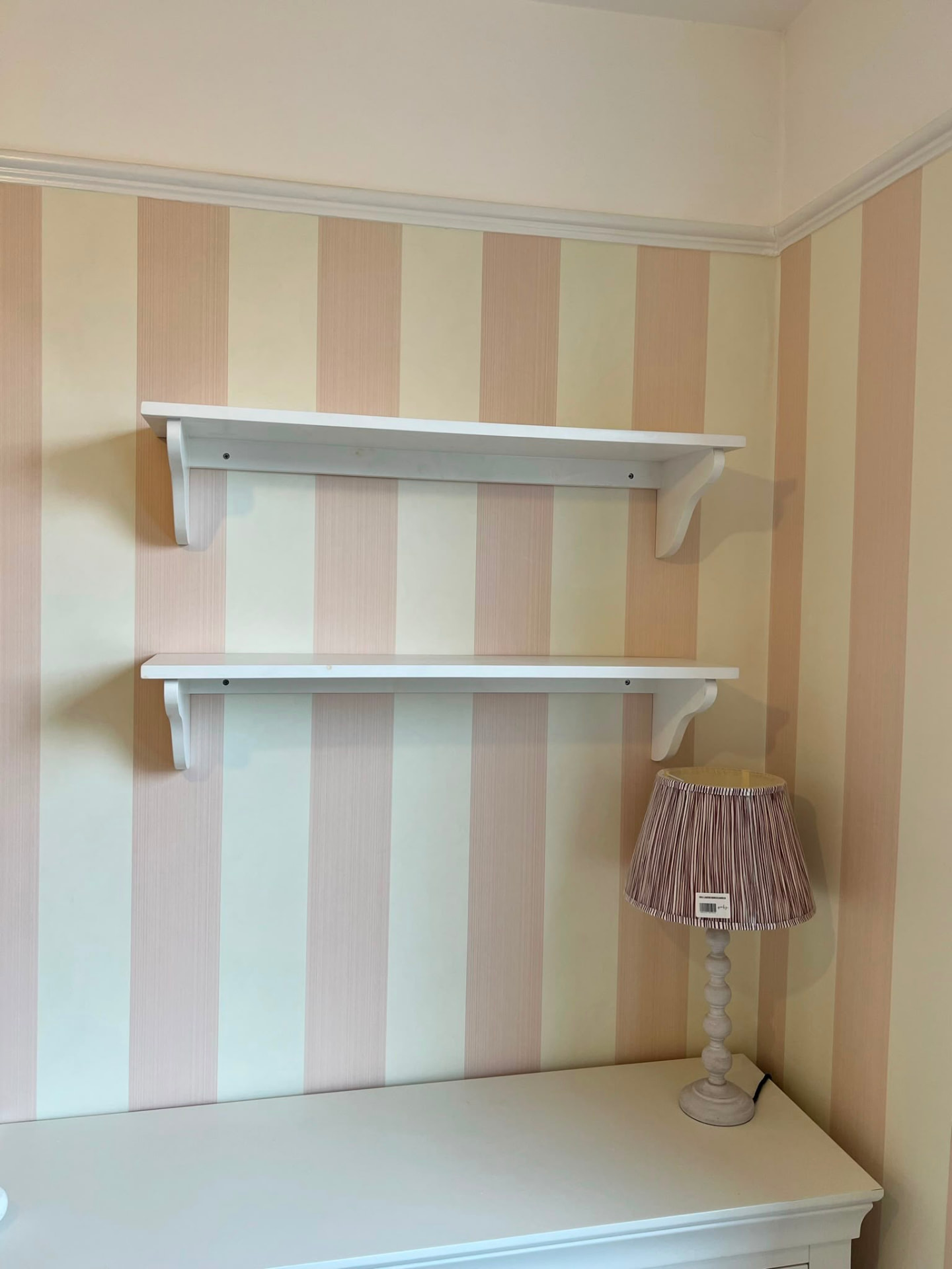 Two white floating shelves fitted to a striped wallpapered wall.
