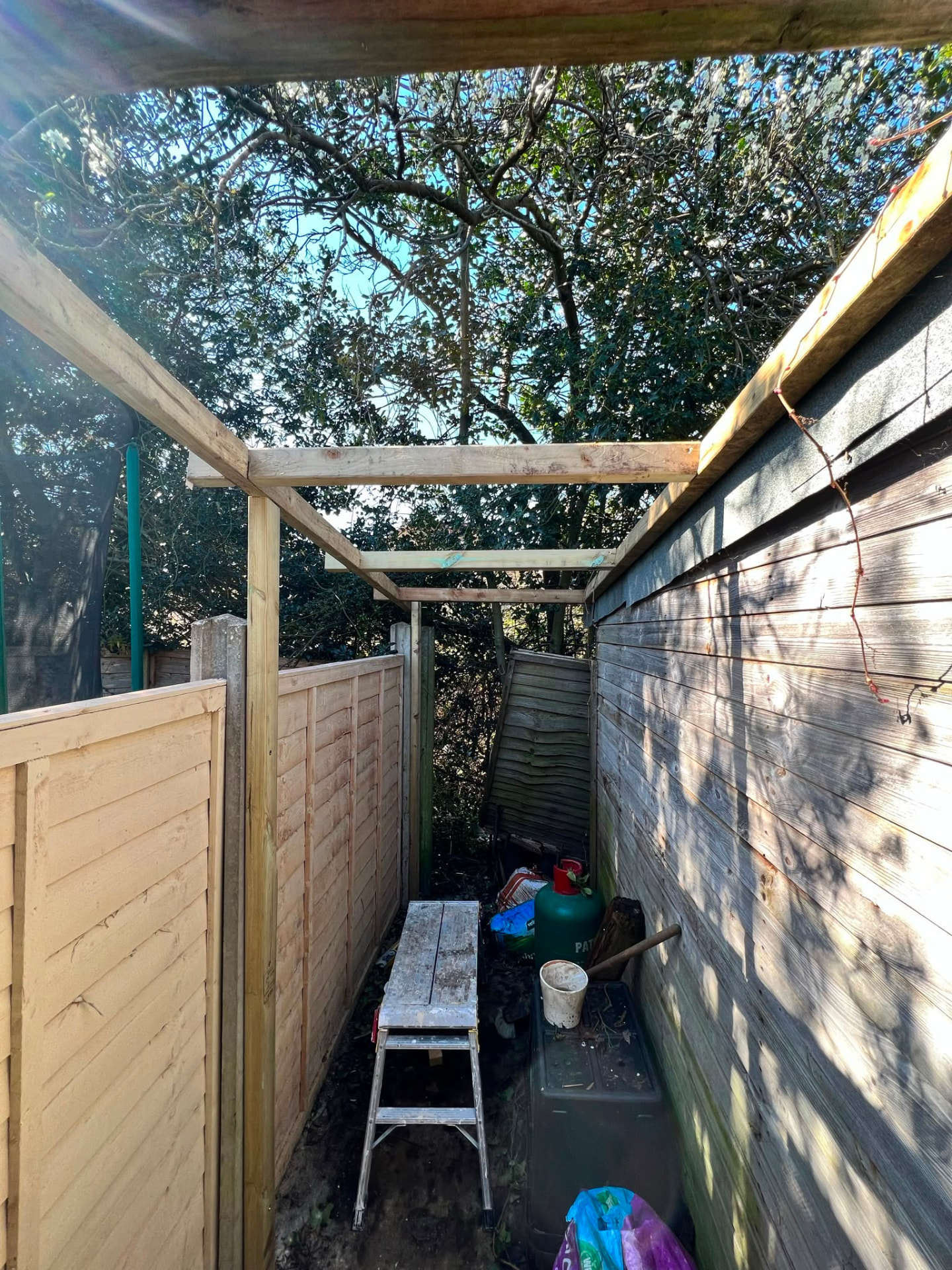 A new timber frame structure being built beside a garden fence.
