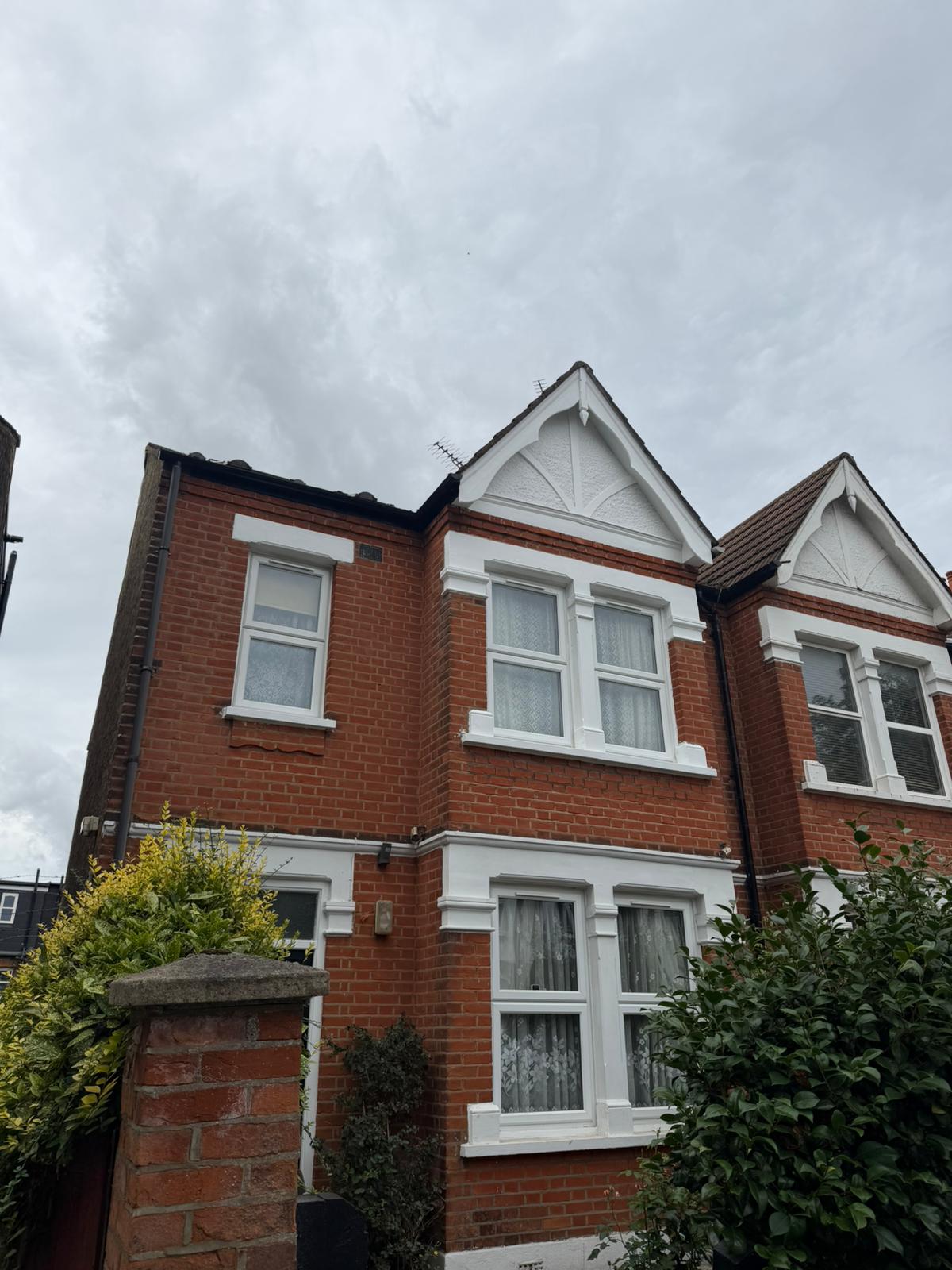 After: the same house exterior with the gable and window trims repainted in a clean white finish.