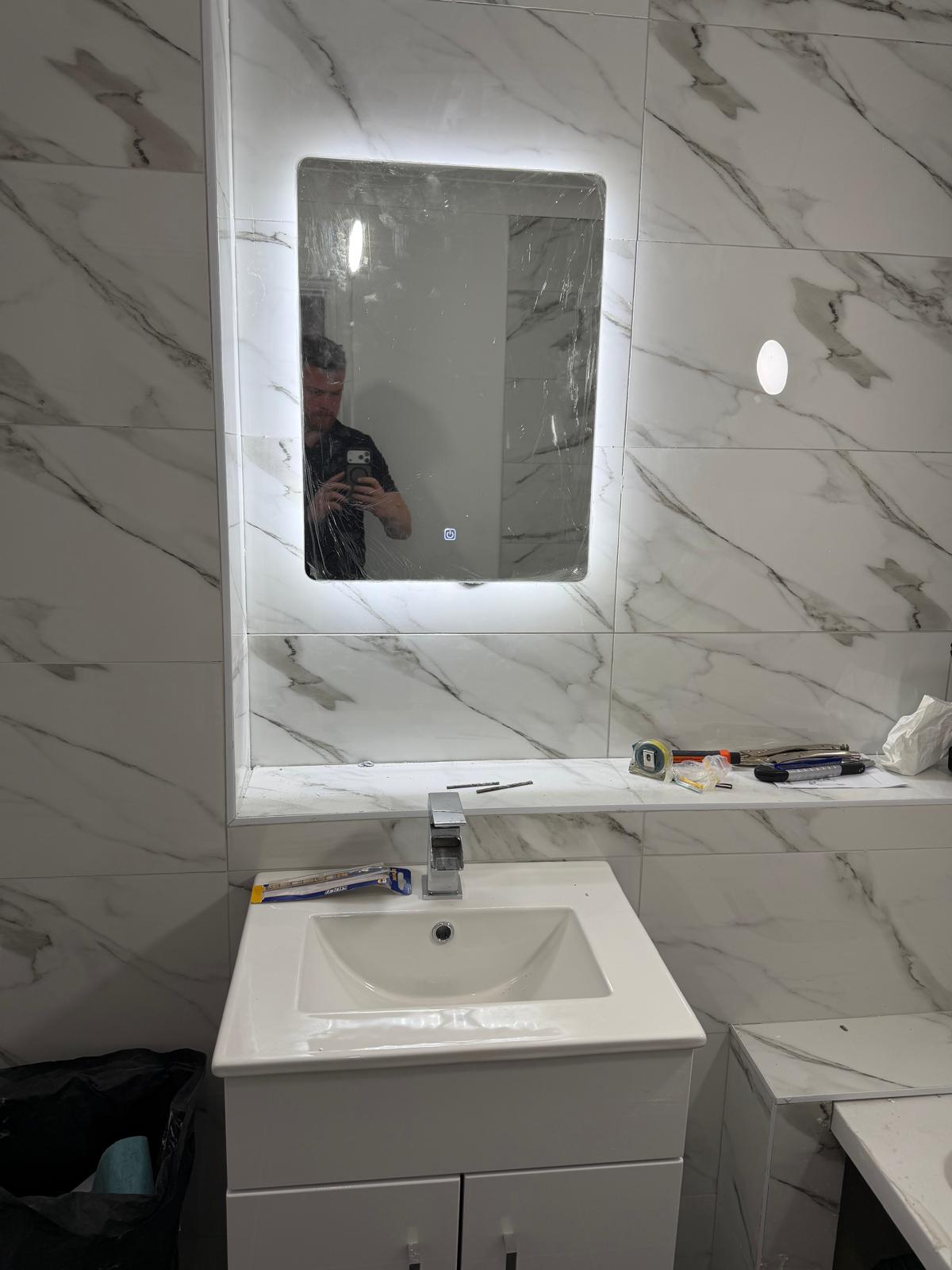 A modern backlit rectangular mirror above a white vanity basin.