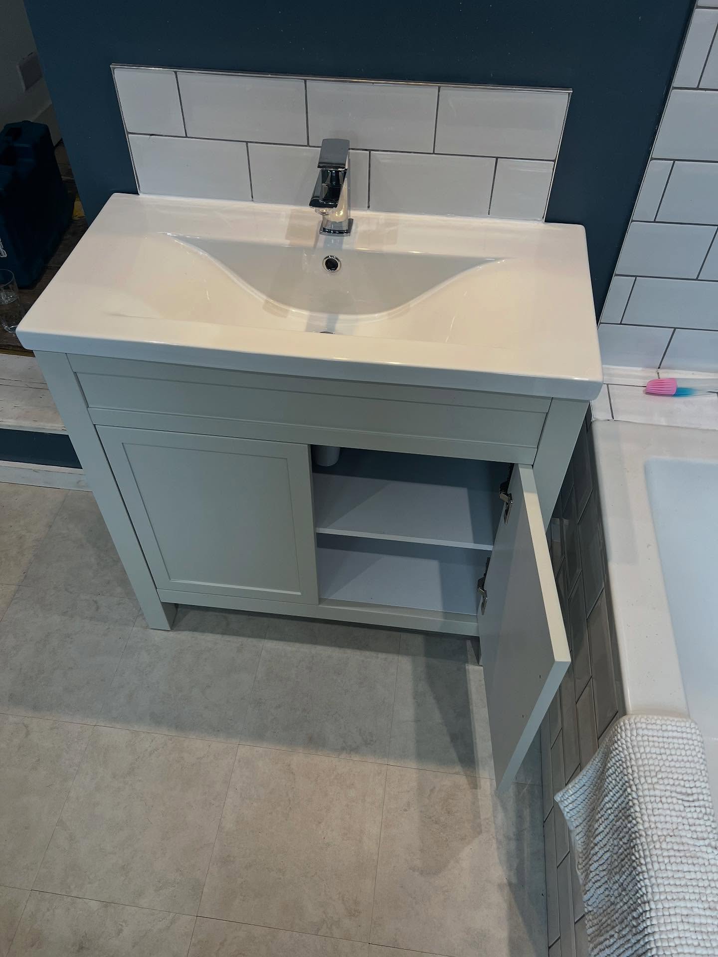 A newly fitted white basin on a pale vanity unit with a tiled splashback.