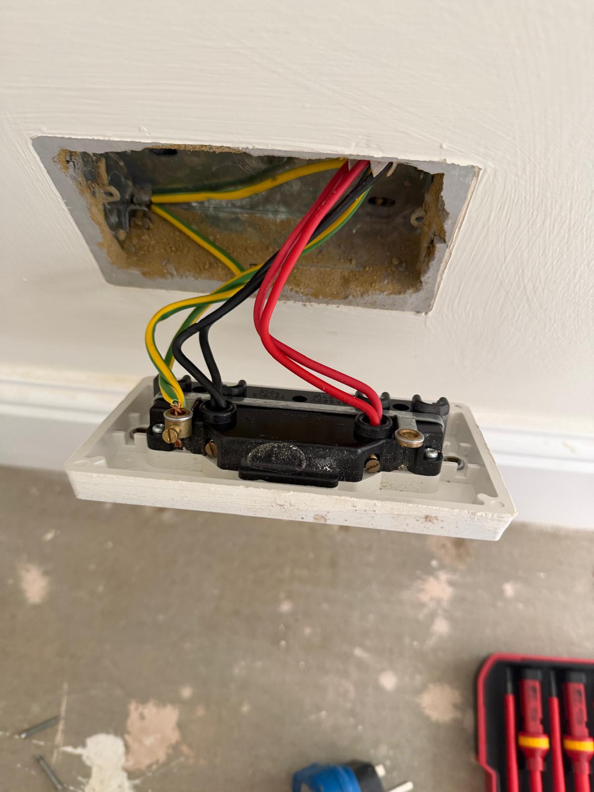 An open electrical wall socket showing the wiring behind it.