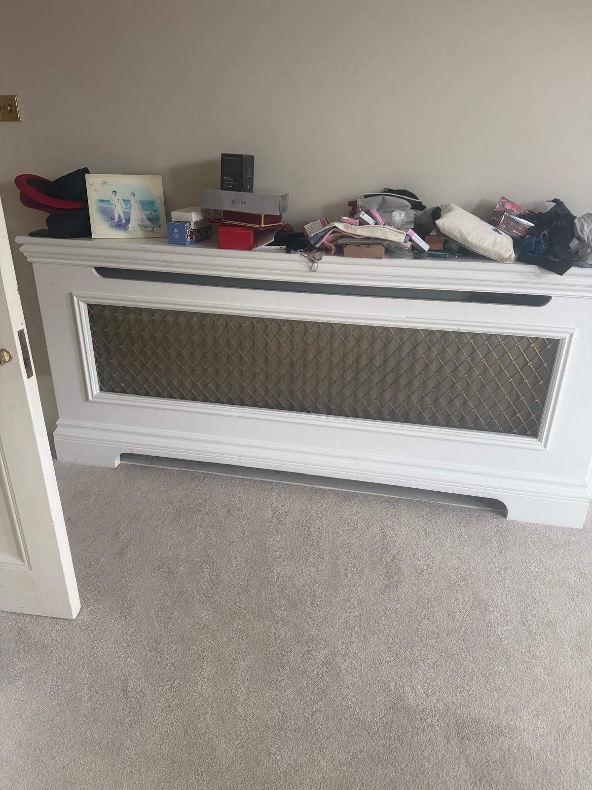 A white radiator cover with a gold mesh panel in a carpeted room.