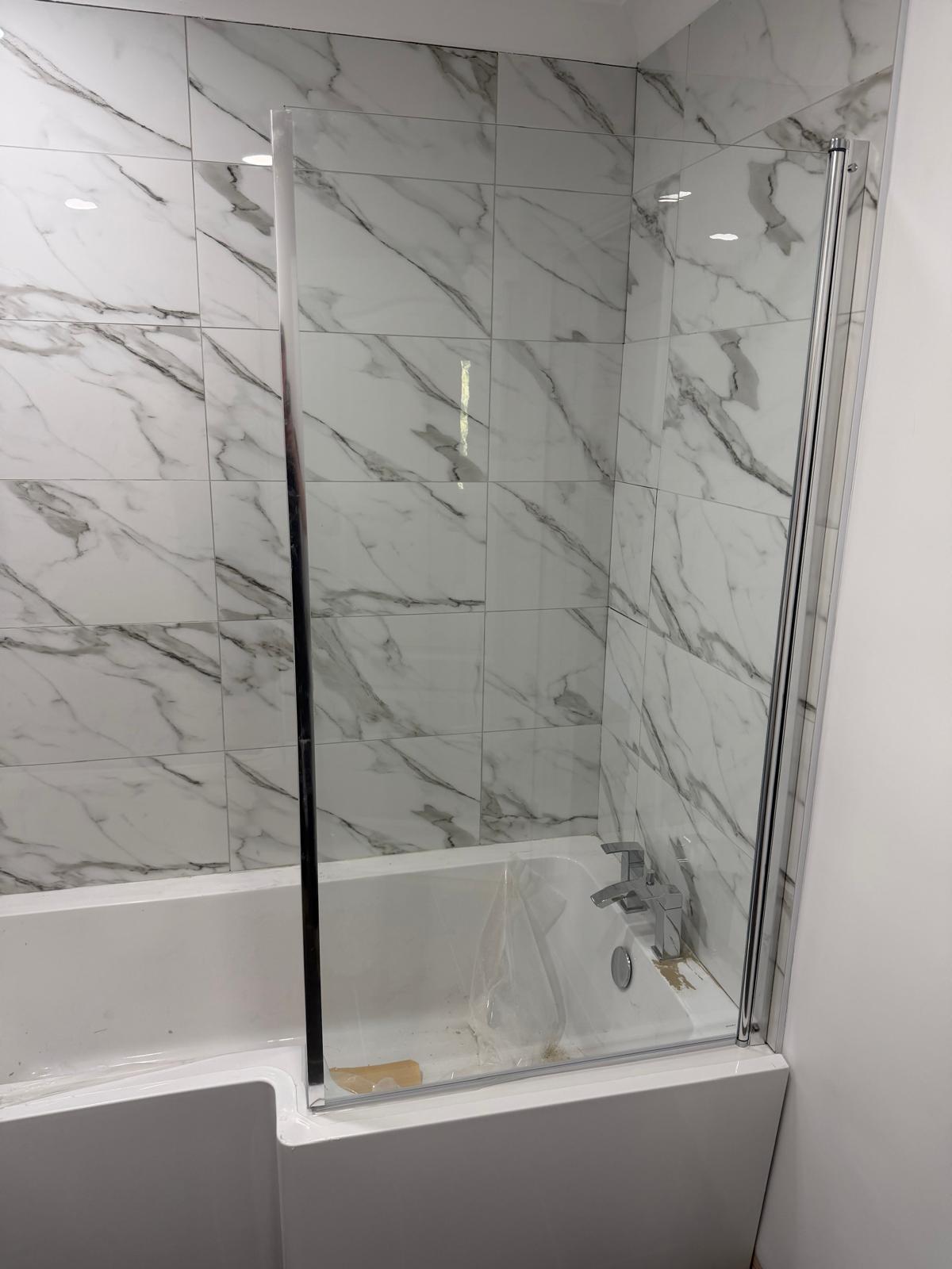 A newly fitted glass shower screen on a bathtub with marble-effect tiles.